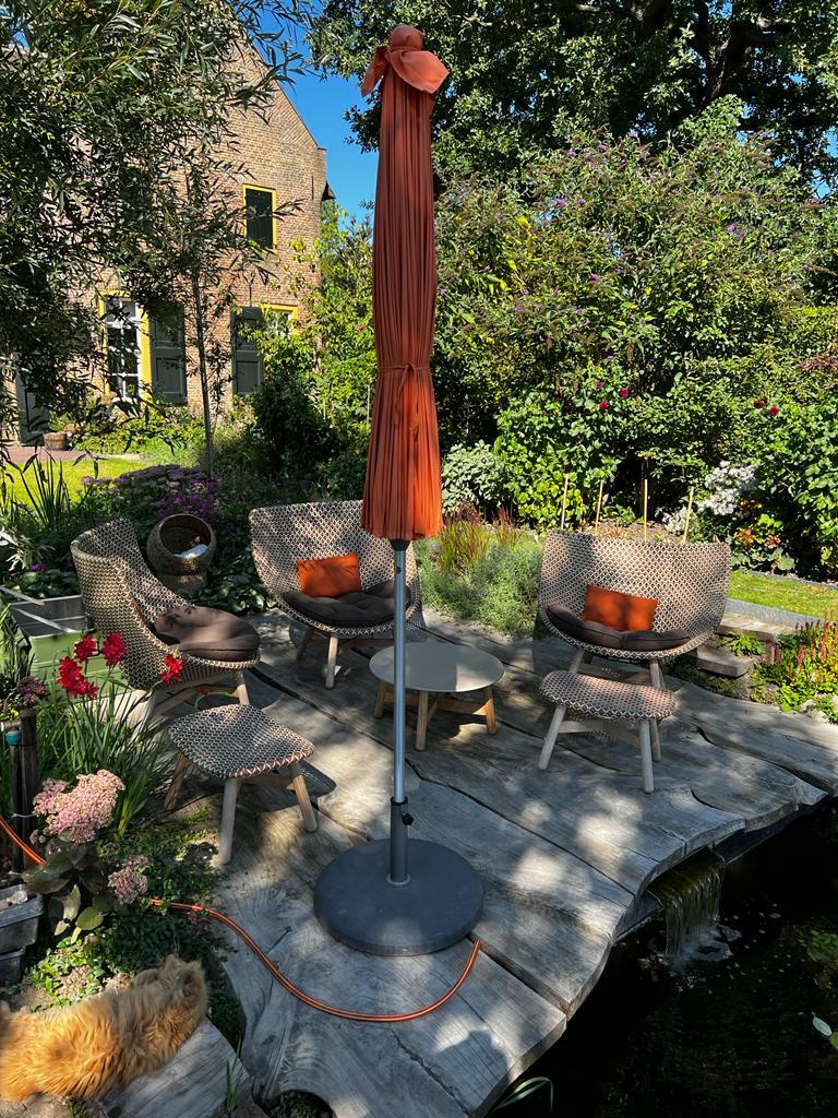 Tuin met meubels en gesloten parasol, zonnige dag.