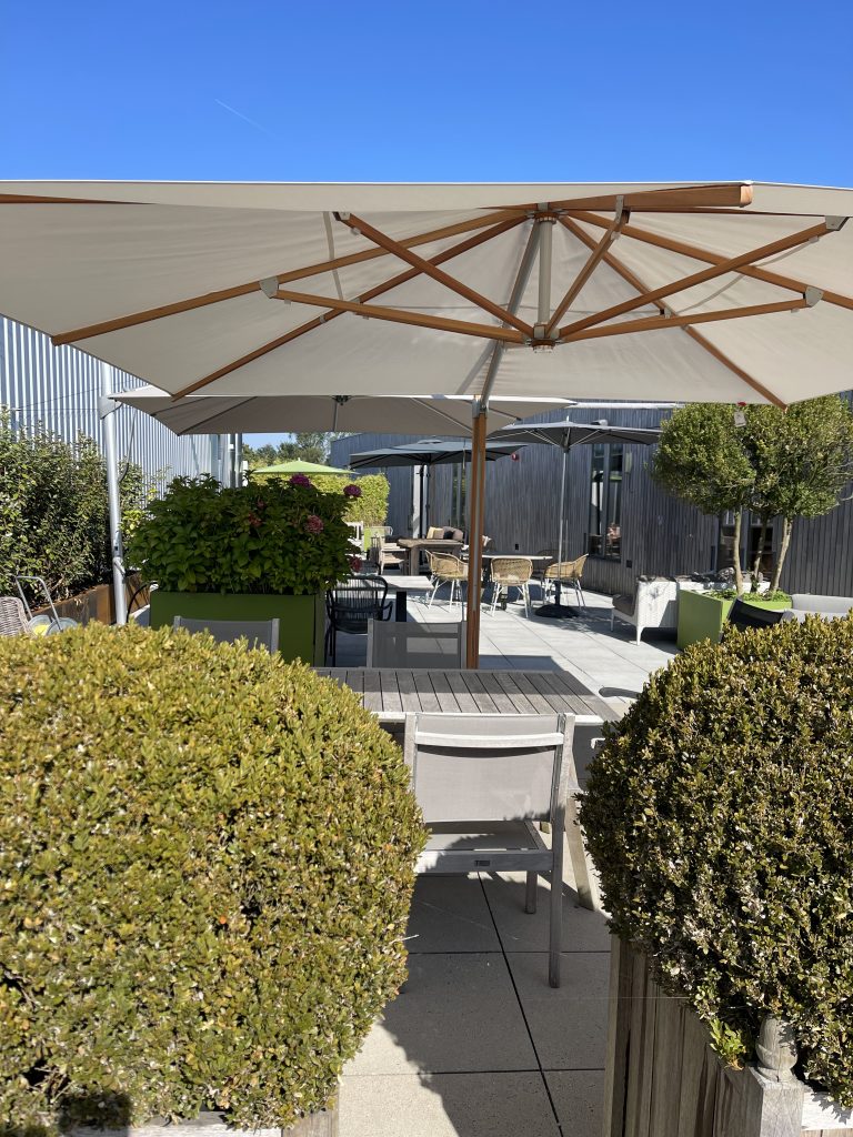 Zonnig terras met tafels en stoelen onder parasol.