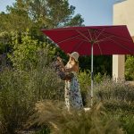 Vrouw plukt bloemen onder een parasol in tuin.