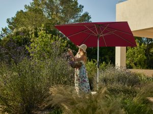 Vrouw plukt bloemen onder een parasol in tuin.