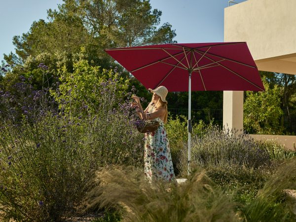 Vrouw plukt bloemen onder een parasol in tuin.
