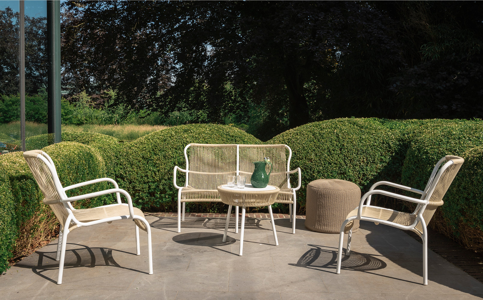 Moderne tuinmeubelen op terras met groene heggen.